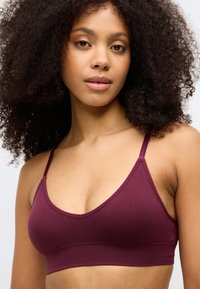 Bralette em bordeaux com nervuras, alças ajustáveis e design em V. Textura suave, acabamento sem costura e uma faixa larga na parte inferior para suporte.