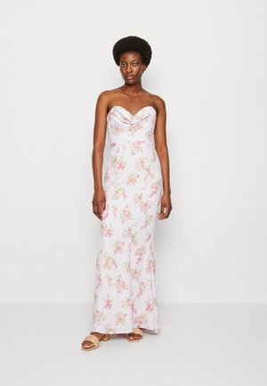 Bezramenné kvetinové šaty v svetloružovej farbe, s draped výstrihom, priliehavým strihom a zložitými kvetinovými vzormi. Skombinované so svetlými sandálmi.