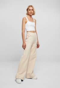 Hvit avkortet tanktopp og lysebeige vide bukser laget av mykt stoff, med elastisk midje og detaljer i sidesømmen.
