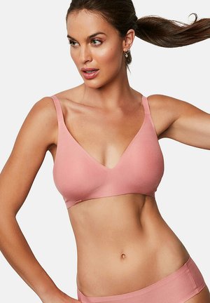 Femme portant un bralette rose poudré sans coutures et des sous-vêtements assortis, les cheveux tirés en une queue de cheval haute.