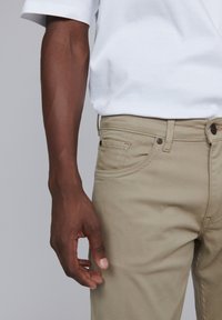 Pantalons en coton kaki avec poches latérales, détails de couture visibles et texture lisse. Associés à une chemise blanche à manches courtes unie.