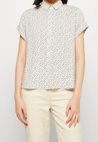 Korte mouwen button-up shirt in crème met een bloemenpatroon. Beschikt over een kraag, een ontspannen pasvorm en lichtgewicht stof.