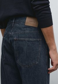 Mörkblå denimjeans med en jämn yta och ett lädermärke på bakre linningen. Har två bakfickor och kontrasterande sömmar.