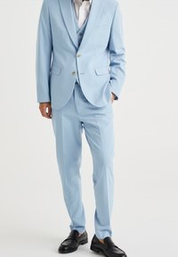 Jasnoniebieski garnitur z dopasowaną marynarką, pasującymi spodniami i białą koszulą. Czarna loafersy dopełniają strój. Gładka faktura tkaniny.