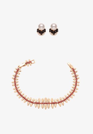 Złota bransoletka z czerwonymi kamieniami szlachetnymi i ozdobami w kształcie złotych liści, zestawiona ze złotymi kolczykami z perłami i czarnymi prostokątnymi kamieniami.