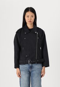 Black suede motorcycle jacket with a belted waist, zippered front, shoulder epaulets, and multiple pockets. Styled with blue jeans.