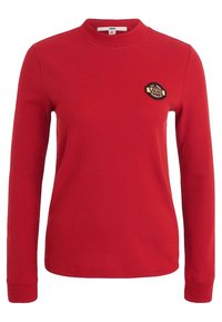 Roter, langärmliger Rippenpullover mit hohem Kragen und einem runden schwarzen und goldenen Vans-Logo-Patch auf der linken Brust.