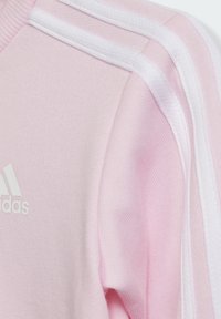 Felpa rosa con strisce bianche sulle spalle, realizzata in tessuto morbido. Presenta un piccolo logo bianco sul petto e un colletto a costine.