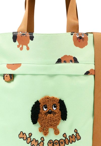 Borsa a mano verde chiaro con manici marroni, decorata con più cani marroni a fumetti con orecchie nere e testo "mini codini" in filato nero e marrone.