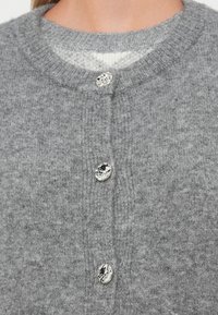 Grå strikket cardigan med rund hals, tre dekorative knapper og en myk tekstur. Knapper med blank sølvfinish.