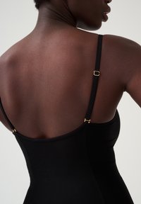 Body nero con sottili spalline e dettagli in hardware dorato. La texture liscia e il design aderente mettono in risalto la schiena.