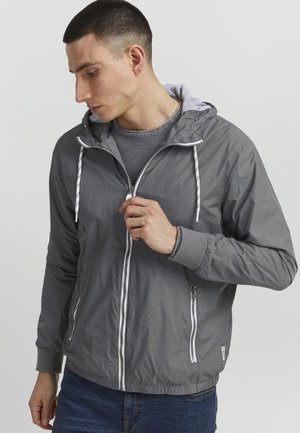 Gray lightweight jacket with a hood, white zipper, and adjustable drawstrings. Features elastic cuffs and a textured gray inner layer.