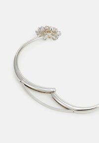 Silver metal bracelet with a curved design, featuring a floral accent made of clear and gold elements, smooth texture, and polished finish.