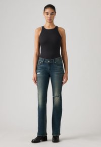 Body noir sans manches associé à un jean bleu à l'aspect délavé avec un genou usé, complété par des bottes noires à talons.