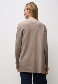 Beige stickad cardigan med en avslappnad passform, ribbade ärmslut och nederkant, samt en slät textur, visad från baksidan mot en enfärgad bakgrund.
