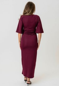 Burgundská maxi šaty s priliehavým telom, rozšírenými rukávmi a hladkou textúrou. Vyznačujú sa nahrnutým dizajnom na zadnej strane a rovnou spodnou líniou.