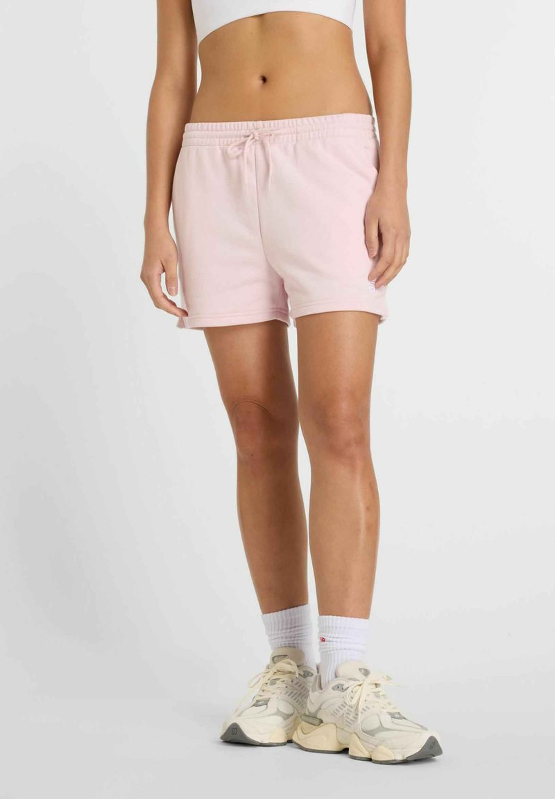 Pantalones cortos de algodón rosa claro con cintura elástica y cordón, que cuentan con bolsillos laterales y un ajuste relajado, combinados con zapatillas blancas.