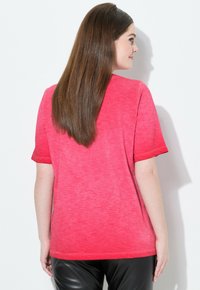 Camiseta de manga corta rosa con un ajuste relajado, que presenta una tela ligeramente texturizada y un escote redondo. La vista trasera muestra el dobladillo y las mangas suaves.
