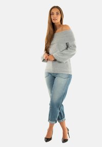 Maglione grigio a spalla scoperta con scollo a costine, abbinato a jeans azzurri arrotolati e tacchi alti neri.