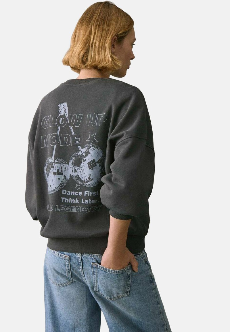 Dunkelgrauer Sweatshirt mit einem Grafikdesign von Discokugeln und dem Text „GLOW UP MODE“ auf der Rückseite. Lässige Passform mit gerippten Bündchen und Saum.