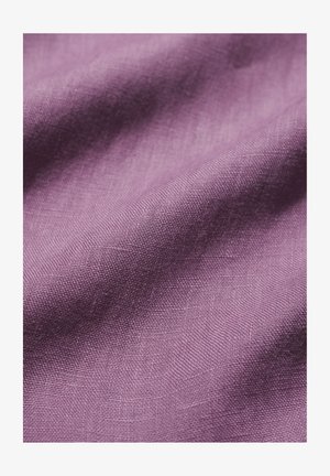 Povečavni posnetek mehke, teksturirane vijolične tkanine z vidnim vzorcem tkanja in nežnimi pregibi, ki ustvarjajo globino in senco.