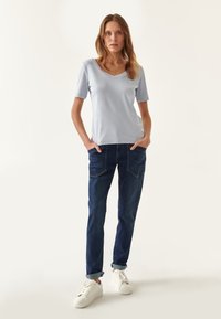 Top azul claro de manga corta y escote en V, combinado con jeans de mezclilla azul oscuro. La modelo lleva zapatillas blancas. Diseño simple con un corte relajado.