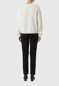 Biały dziany sweter o luźnym kroju, szerokich rękawach i ściągaczu na dole, zestawiony z dopasowanymi czarnymi spodniami i czarnymi botkami za kostkę.