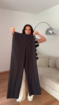 Pantalones anchos de rayas oscuras con una cintura alta y dos bolsillos frontales, sostenidos en una habitación bien iluminada.