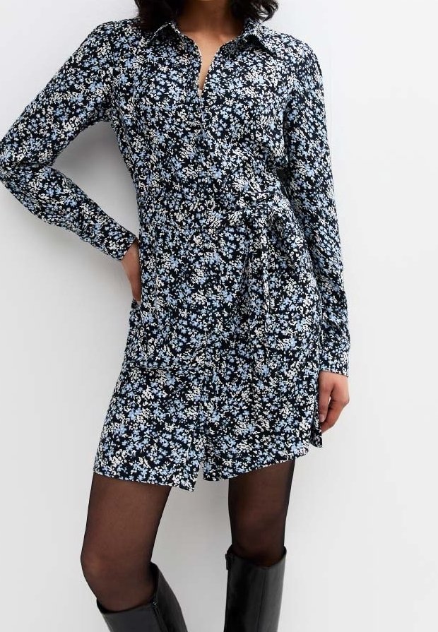 Vestito camicia a maniche lunghe di colore blu scuro con un piccolo motivo floreale bianco e azzurro. Chiusura con bottoni frontale, scende sopra il ginocchio e si allaccia in vita.