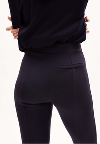 Zwarte high-waisted leggings, rekbaar materiaal, gladde textuur, met een klein achterzakje en een getailleerde pasvorm. Geen zichtbare patronen of accenten.