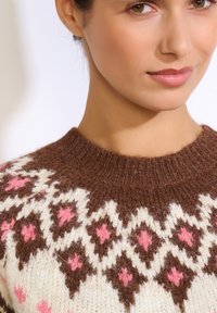 Hnedý vlnený sveter s okrúhlym výstrihom, ozdobnými bielymi a ružovými diamantovými vzormi a jemným textúrovaným povrchom.