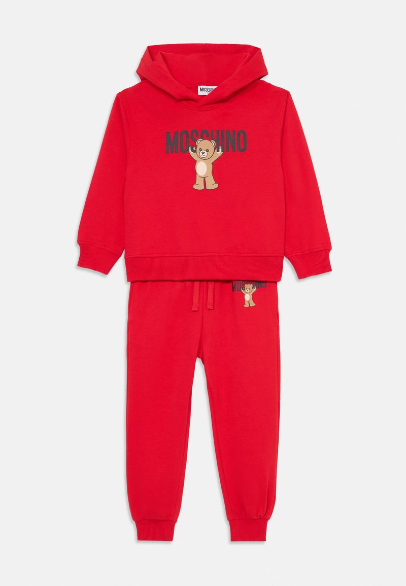 Sarkana kapuce un sporta bikses komplekts, kas izgatavots no mīkstas auduma. Priekšpusē ir lāča grafika, kā arī elastīgas aproces biksēm. Klātesošs "Moschino" logo.