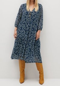 Námořnické květinové šaty s dlouhými průsvitnými rukávy, vrstvenou sukní a véčkovým výstřihem; doplněné o hnědé boty po kolena.