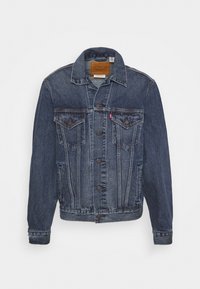 Chaqueta de mezclilla en azul oscuro con cierre de botones, dos bolsillos en el pecho y un collar clásico. Presenta una etiqueta tejida en el cuello trasero.