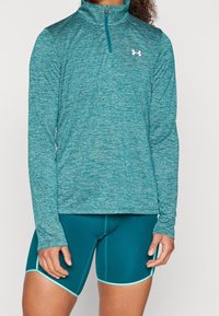 Teal långärmad ziptröja i texturerat tyg, i kombination med figursydda teal shorts med kontrasterande ljusblå kant.