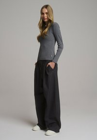 Szara bluzka z długim rękawem w połączeniu z luźnymi czarnymi spodniami. Strój charakteryzuje się luźnym krojem, miękką teksturą i subtelnym detalem z logo.