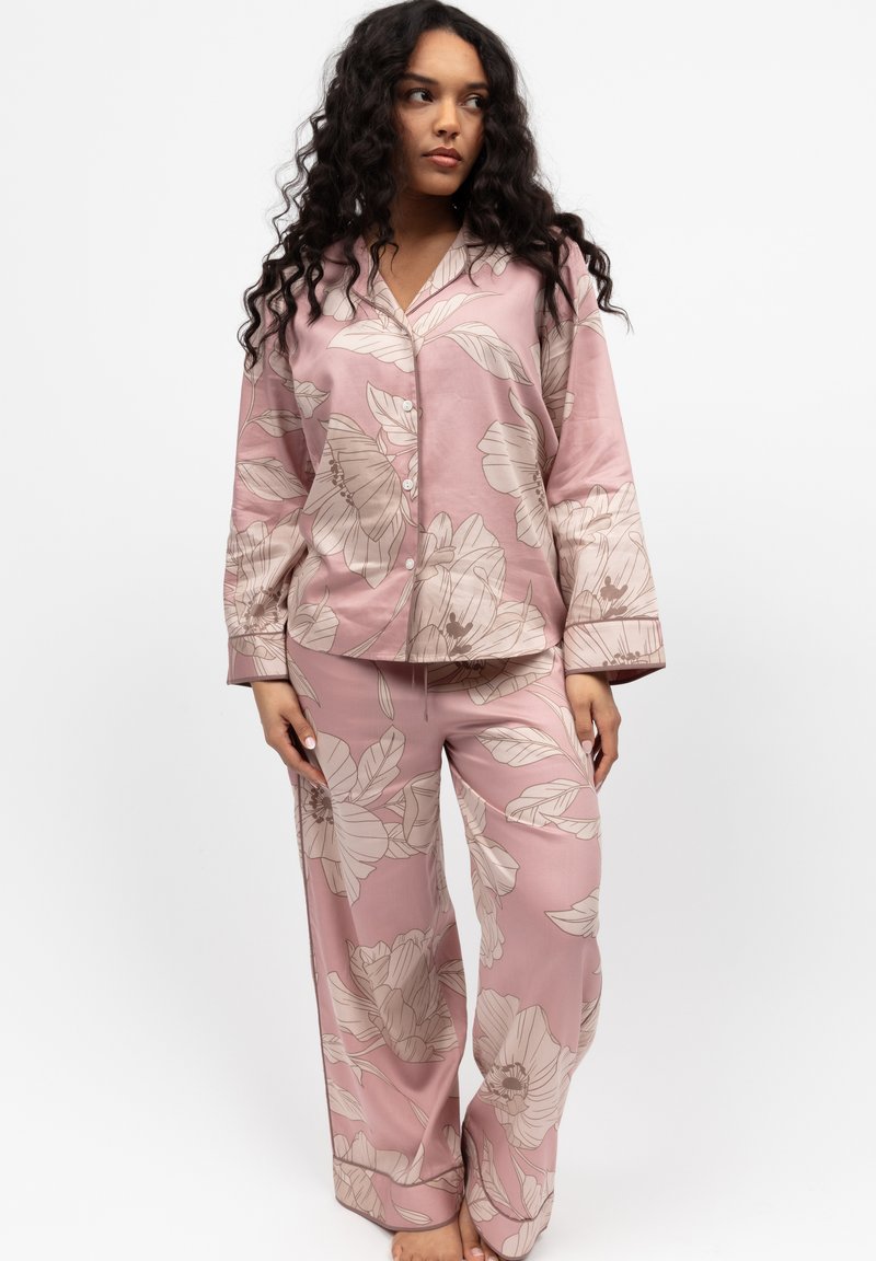 Rosa Pyjama-Set mit floralen Mustern, bestehend aus einem langärmeligen Oberteil mit Knöpfen und locker sitzenden Hosen mit großen, hellbeigen Blumenmustern und weicher Textur.