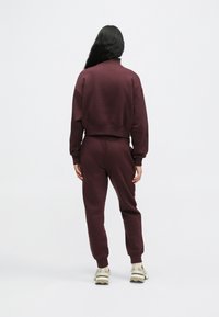 Bordeau-pusakka, jossa on korkea kaulus ja ribbireunat, yhdistettynä yhteensopiviin verkkareihin. Asusteessa on rento leikkaus ja teksturoitu kangas.