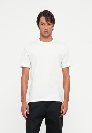 White cotton t-shirt with short sleeves, round crew neck, and a classic fit. Worn with black pants, featuring a plain and smooth texture.