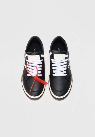 Sneakers in pelle nera con lacci bianchi, dotati di un'etichetta rossa, punta rotonda e suola bianca a contrasto. Pannello decorativo sul lato.