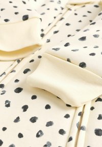 Hoodie à fermeture éclair de couleur jaune pâle avec un motif moucheté noir et gris, poignets côtelés et texture de tissu douce.