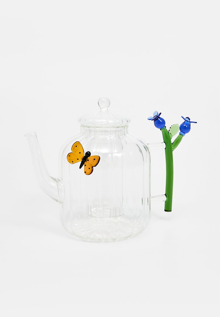 Przezroczysty szklany czajnik o zaokrąglonym kształcie, z pomarańczowym akcentem w kształcie motyla i zieloną rączką ozdobioną niebieskimi kwiatami.