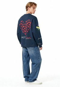 Temno modra majica s kapuco, na hrbtni strani z velikim rdečim srcem in besedilom "SWEET heart" spodaj. Okrašena z cvetličnim vzorcem na rokavu.