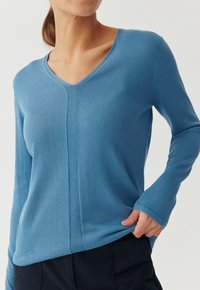 Blauer langärmliger V-Ausschnitt-Pullover aus geripptem Strickstoff, mit einer Mittelnaht und leicht ausgestellten Bündchen für eine lockere Passform.