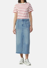 Gestreepte rood-witte t-shirt gecombineerd met een lichtblauwe denim midirok, met twee voorzakken en een rechte snit. Witte sneakers.