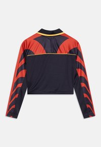 Langermet crop topp i marineblå med røde og svarte bølgemønstre. Har en gul aksentlinje langs ryggen og en klassisk krage.