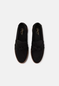 Mustad nubukist slip-on kingad, mille ees on sõlmega detail, pehme sisetallaga ning kontrastse pruuni tallaga.