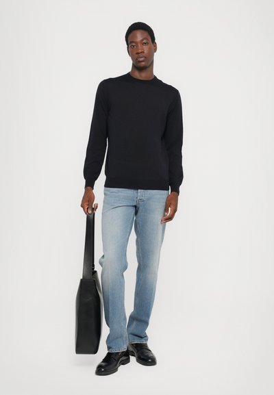 Black knitted sweater, light blue jeans, black leather shoes, holding a black leather bag. Simple design, fitted shape, no patterns.