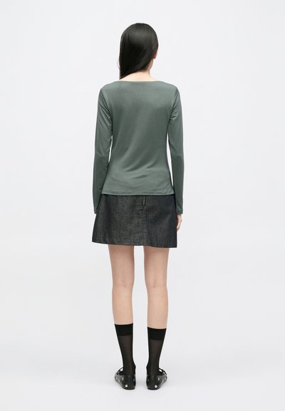 Top verde de mangas longas feito de um tecido suave, combinado com uma saia de ganga preta. Modelo usa meias até ao tornozelo pretas e sapatos com tachas.