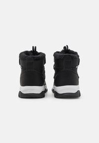 Schwarze High-Top-Schuhe mit einem strukturierten schwarzen Fellfutter, kontrastierender weißer Sohle, Zuglasche und verstellbaren Riemen.